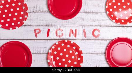 Disposable paper dishes for a picnic with red polka dots and stripes - plates, cups and cutlery. View from above. Stock Photo