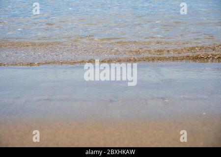 Wave reaching a calm sandy beach. Front view close-up. Ground level view. Blurred background. Stock Photo