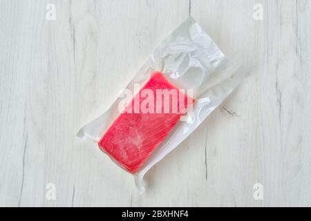 Raw frozen tuna fillet in vacuum packaging on wooden background Stock Photo