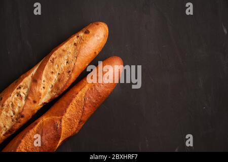 Two crispy french baguettes lie dark black table background sesame seeds Classic french national pastries Copy space Concept for menu or advertising Stock Photo