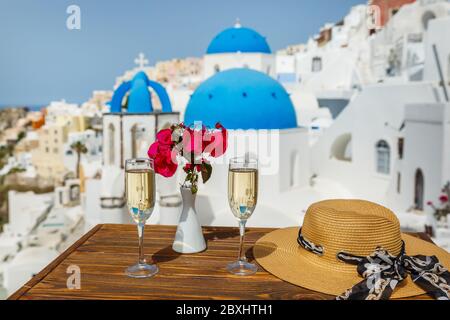 Two glasses of white wine and a hat on the table, against the backdrop of the island of Santorini Stock Photo