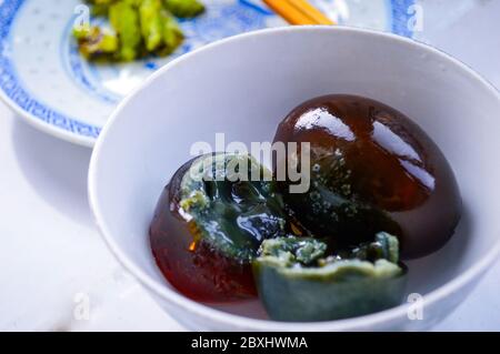 Chinese Century Eggs in White Bowl. One Egg Cut in Half Shows Black Soft Yolk Inside. Stock Photo