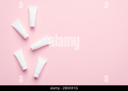Blank white cosmetic tubes on pink background. Packaging cream containers design. Flat lay, top view. Stock Photo