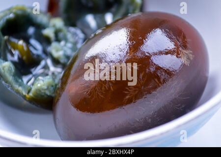 Closeup of Chinese century eggs in white bowl. The egg white is half transparent and shows the snowflake patterns. Blurred soft yolk at background. Stock Photo