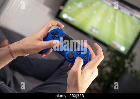 man hands holding joystick and playing video game at home on coach sofa in front of television with play game concole Stock Photo