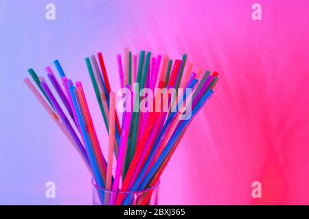 Disposable plastic multicolored tubules for drinks in glass on neon background, copy space. Festive concept, party, birthday. Flat lay, top view. Hori Stock Photo