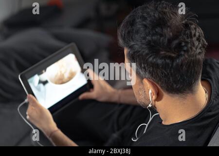 man hand holding using digital tablet watching online cooking master class using headphones. learning cooking remotely Stock Photo
