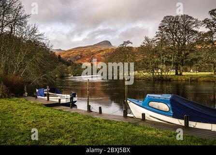 Two boats moored at the private jetty on River Dochart in Killin, with one of the peaks of the Tarmachan ridge in the background. Stock Photo