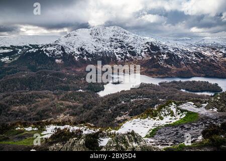 Winter Scottish view from Ben A'an overlooking Loch Katrine and snow-capped peak of Ben Venue in Scottish Highlands.