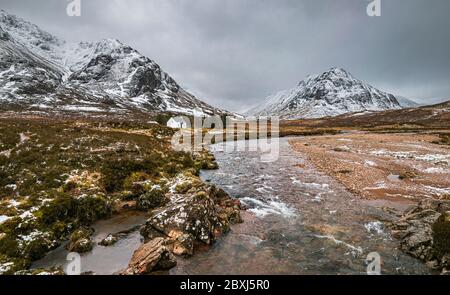 Picturesque winter landscape of Glen Coe with the iconic white cottage against the backdrop of Buachaille Etive Mor and stormy clouds on the horizon. Stock Photo