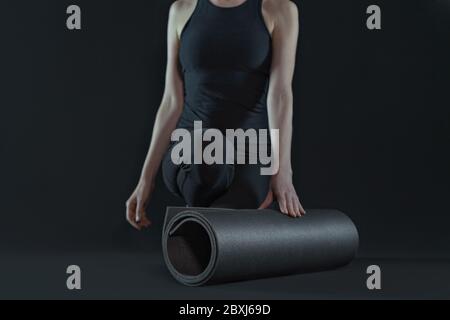 Young woman with yoga mat practicing yoga on dark black background. front view Stock Photo