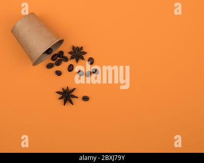Paper Cup, coffee beans and anise stars on an orange background. Stock Photo