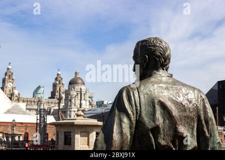 Detail of The Emigrants statue by Mark de Graffenried with historic waterfront buildings in background, Albert Dock, Liv Stock Photo