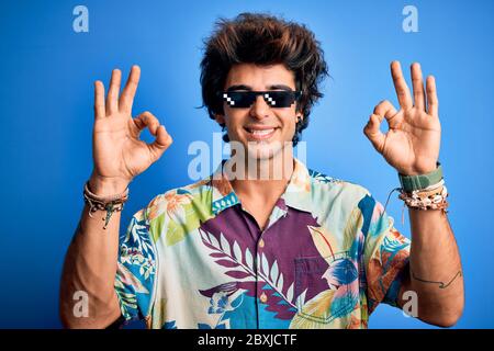 Young handsome man wearing thug life glasses standing over isolated blue background relax and smiling with eyes closed doing meditation gesture with f Stock Photo