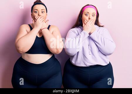 Young plus size twins wearing sportswear shocked covering mouth with hands for mistake. secret concept. Stock Photo