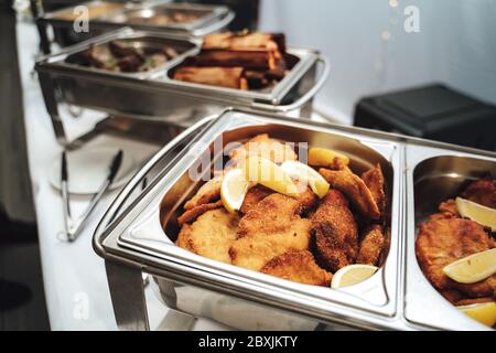 https://l450v.alamy.com/450v/2bxjkty/row-of-stainless-hotel-pans-on-food-warmers-with-various-meals-fried-schnitzel-with-slices-of-lemon-self-service-buffet-table-celebration-party-2bxjkty.jpg