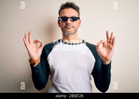 Young handsome man wearing funny thug life sunglasses meme over white background relax and smiling with eyes closed doing meditation gesture with fing Stock Photo