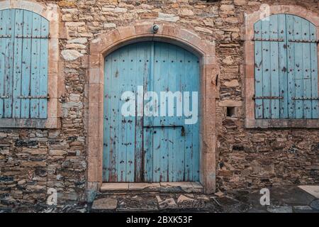 Closed blue wooden door and windows in old stone brick Cyprus building exterior. Stock Photo