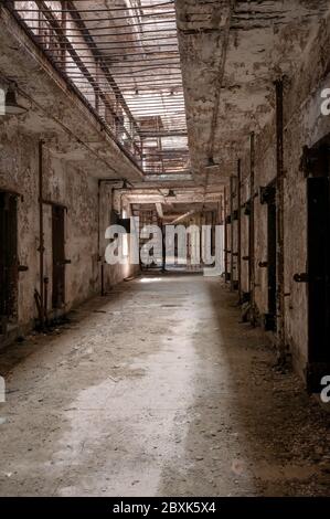 Hallway of an old abandoned prison showing doorways to cells, metal stairs, and bars on the ceiling. Stock Photo