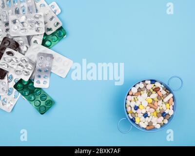 Empty blisters and a lot of pills in the container on the blue background. Stock Photo