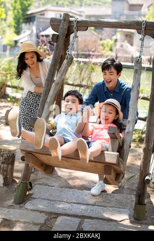 Happy young Chinese family playing on swing Stock Photo