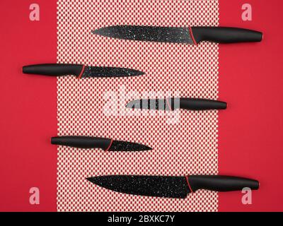 A set of kitchen knives on a white doily on a red background. Stock Photo