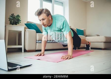 Blonde caucasian man with bristle doing push-ups on the floor using a laptop