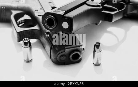 Two black semi automatic pistols, a 40 caliber and a 9mm with a bullet for each next to them on a white background shot in black and white Stock Photo