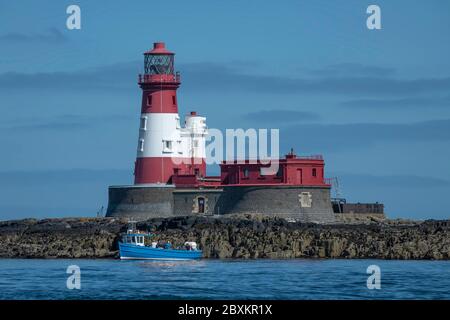 Longstone Lighthouse located in the Farne Islands of the United Kingdom with blue boat in front of it Stock Photo
