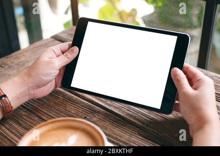 Mockup image of a woman holding black tablet pc with blank white desktop screen with coffee cup on wooden table Stock Photo