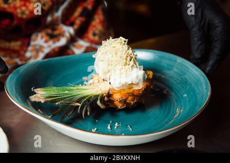 Freshly prepared salad lies inside the pineapple, which is cut lengthwise, sprinkled with grated cheese. Everything looks very appetizing. Stock Photo