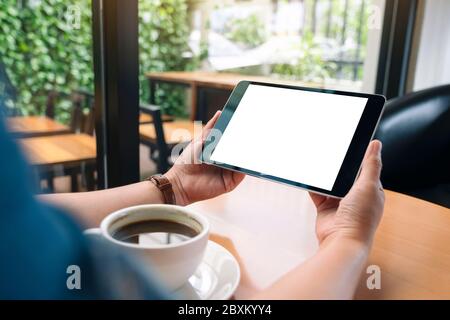 Mockup image of hands holding black tablet pc with blank white screen with coffee cup on wooden table Stock Photo