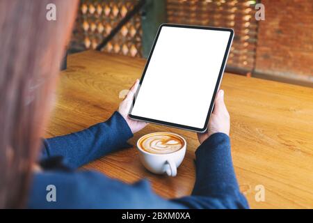 Mockup image of a woman holding black tablet pc with blank white screen with coffee cup on wooden table Stock Photo