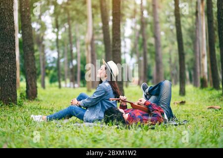 A young couple playing ukulele while sitting and lying down in the woods together Stock Photo
