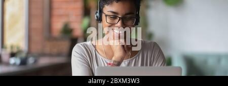 Smiling African girl wear headphones watch online webinar use laptop Stock Photo