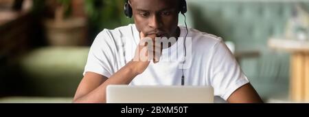 Focused African student wear headphones studying using laptop horizontal photo Stock Photo