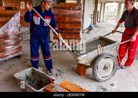 Zrenjanin, Vojvodina, Serbia - April 11, 2018: Construction worker is using shovel to unloading cement, mortar, from wheelbarrow on construction site. Stock Photo