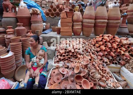 A vendor and her toddler sitting among of hundreds pottery wares for sale at the Pottery Market, north of Indra Chowk, Kathmandu, Nepal, Stock Photo