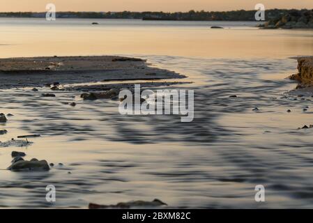 Small stream reaches the sea and freshwater flow through the river. Small stream flows into the sea through the beach. Stock Photo