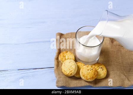 jug and glass of milk on a blue wooden background with cookies Stock Photo