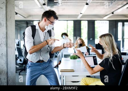 Young people with face masks back at work in office after lockdown, having fun. Stock Photo
