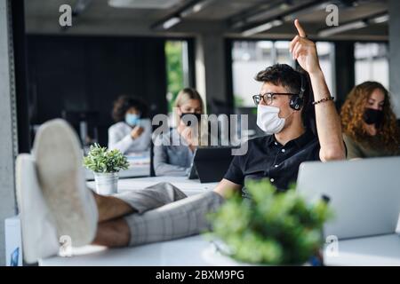 Young people with face masks back at work or school in office after lockdown, having fun. Stock Photo