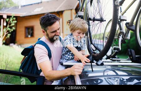 Father with small son putting bicycles on car roof, going on trip concept. Stock Photo