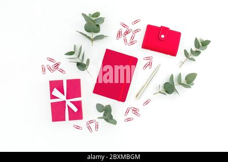 Red notebook, gift box, pen and clips with eucalyptus on white background. Flat lay. Stock Photo