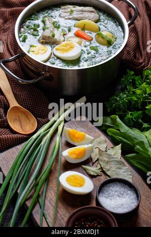 Polish sorrel soup of fresh sorrel, green onion, parsley with pork ribs, young potato, carrot, and boiled eggs, on a wooden table with ingredients: pa Stock Photo