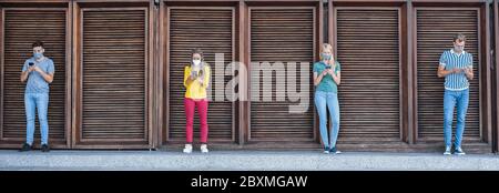 Young people wearing face safety masks using smart mobile phones while keeping social distance during coronavirus time - Technology and covid-19 sprea Stock Photo