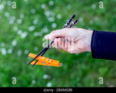 A female hand holds two Japanese chopsticks with which she raises a piece of plastic to symbolize the environmental problem Stock Photo