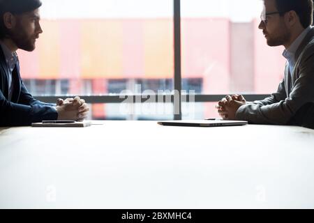 Two serious businessmen sitting at desk looking at each other Stock Photo