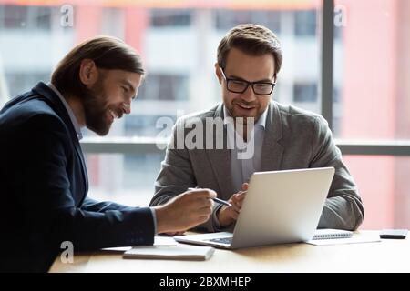 Teammates positive businessmen using laptop learn new corporate app Stock Photo