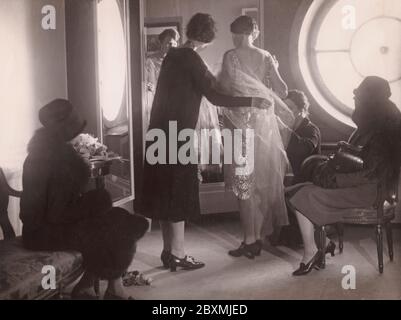 Back in the 1920s. At the department store NK in Stockholm, a woman is standing in front of a mirror trying on a dress. Two women of the staff is adjusting details to make it fit perfectly. Perhaps a dress for a celebration or a party, it is the roaring twenties after all. Stock Photo